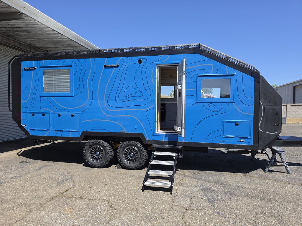 Side profile of the Titan Edition in a blue topographic wrap, entry door open with fold-out steps