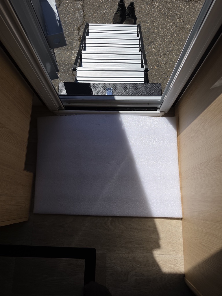 Downward view from the open entry doorway over the diamond-plate step to the ladder on the pavement