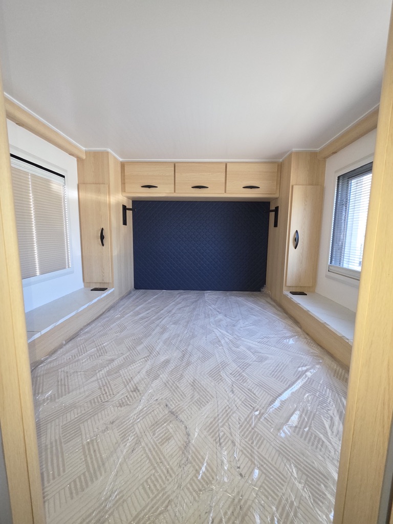 Rear bedroom of the Titan Edition with a navy quilted headboard and oak overhead lockers