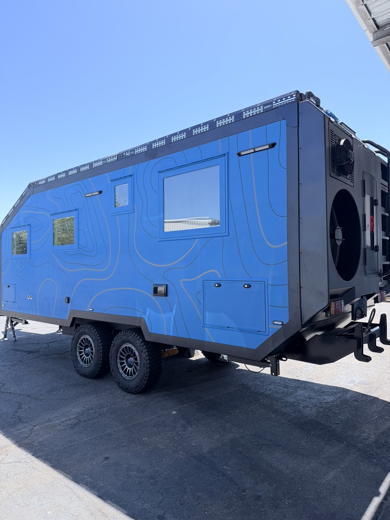 Full side profile showing the topographic-line wrap, tandem axles and rear utility wall with spare tire