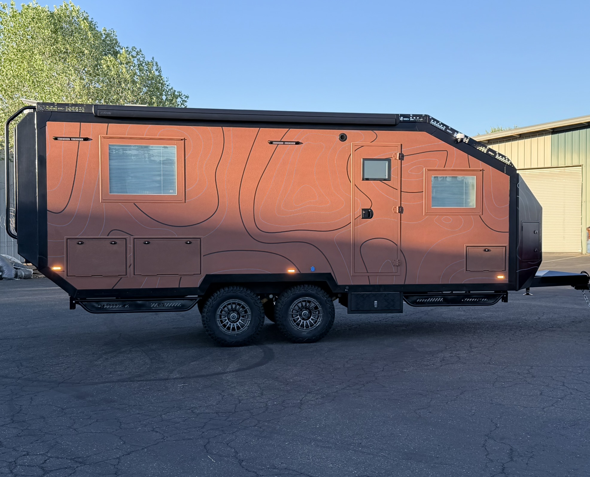 Side profile of the Titan Edition in terracotta topographic wrap, tandem off-road wheels and roof awning